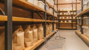 Estanterías con sacos de papel y envases de alimento y una cesta de la compra en el suelo